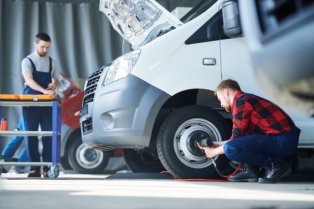 L'un des jeunes professionnels de l'entretien automobile fixant les détails de la roue pendant que son collègue se penche sur la boîte à outils