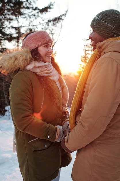 Jeunes rendez-vous souriants en vêtements d'hiver se regardant tout en se tenant par les mains