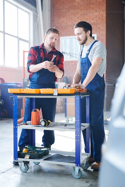 L'un des jeunes réparateurs montrant à son collègue ou stagiaire une nouvelle clé tout en la tenant sur une boîte à outils ouverte