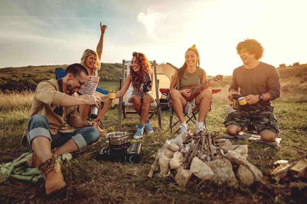 Les jeunes s'amusent bien au camp dans la nature. Ils se reposent, boivent du thé, rient et chantent avec de la musique de ukulélé, heureux d'être ensemble.