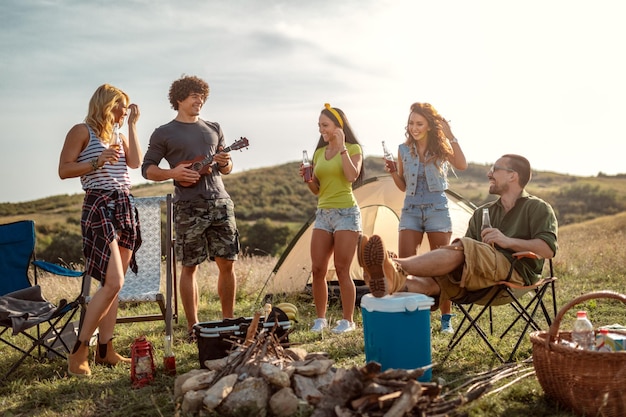 Les jeunes s'amusent bien au camp dans la nature. Ils se reposent, rient et chantent avec de la musique de ukulélé, heureux d'être ensemble.