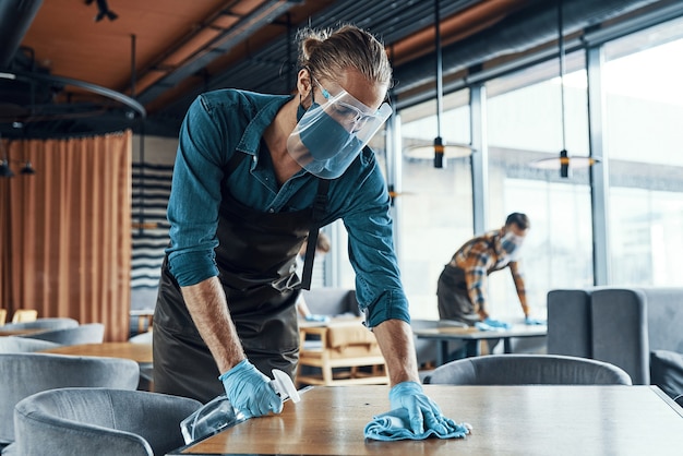 Jeunes serveurs masculins dans des tables de nettoyage de vêtements de travail protecteurs au restaurant