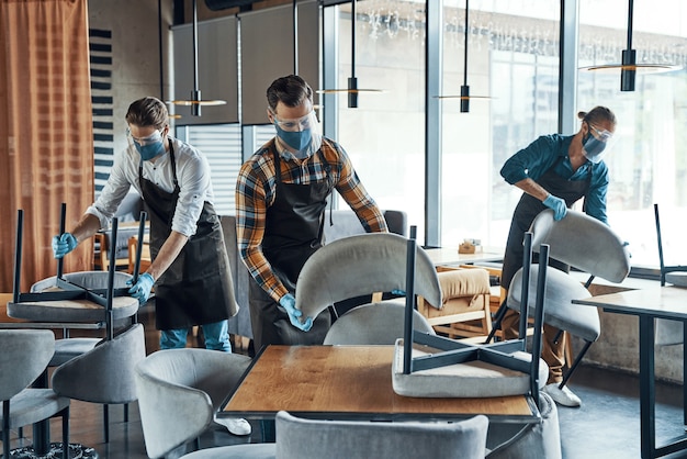 Jeunes serveurs masculins dans des vêtements de travail protecteurs arrangeant des meubles dans le restaurant