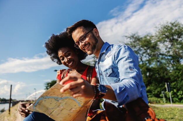 Jeunes touristes multiraciaux assis à l'extérieur et explorant la carte.