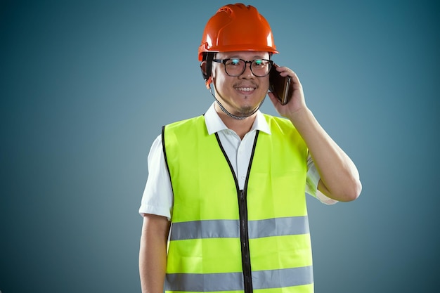 Jeunes travailleurs de la construction asiatiques dans un casque de sécurité et utilisant un smartphone isolé sur fond bleu