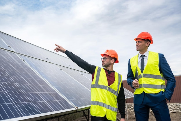 De jeunes travailleurs portant des casques de vestes de travail discutent du plan de travail des panneaux solaires pour l'économie de l'énergie électrique Concept d'électricité verte