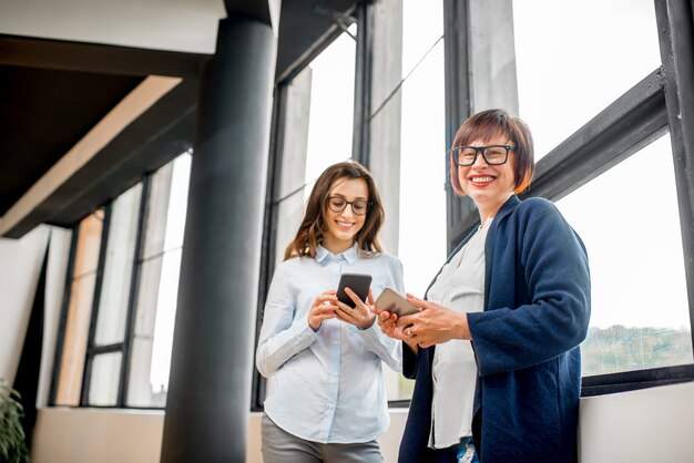 Jeunes et vieilles femmes d'affaires debout près de la fenêtre au bureau