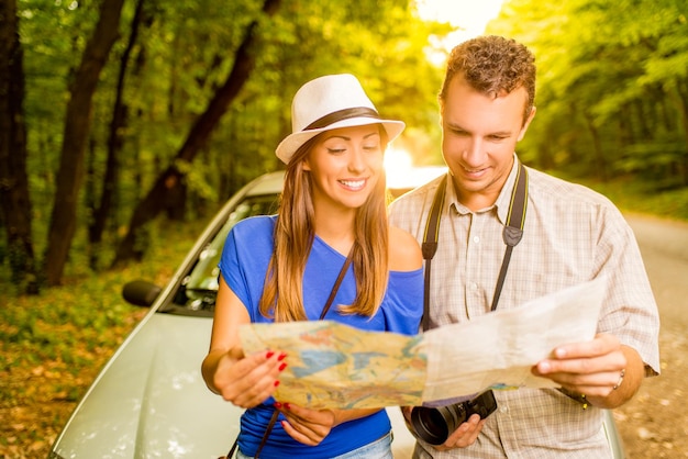 Jeunes voyageurs debout devant une voiture dans la forêt, tenant une carte et recherchant la prochaine destination.