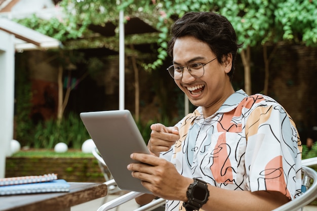 La jeunesse asiatique avec des lunettes tient et regarde l'écran de la tablette puis rit en étant détendue