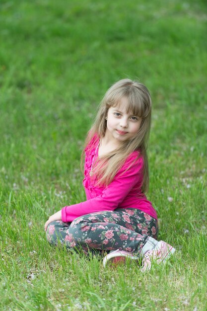 Jeunesse, fraîcheur, enfance. Petite fille sur l'herbe verte, printemps. Enfant aux longs cheveux blonds, beauté. Beauté, mode, look, coiffure. Avenir, croissance, printemps.