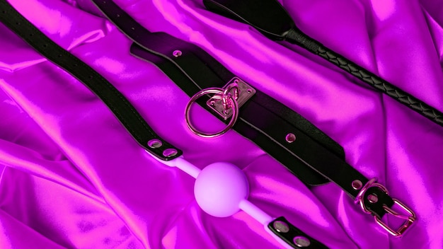 Photo jeux de sexe pour adultes articles bdsm collier en cuir boule de bâillon rose et fouet sur une feuille de satin rouge