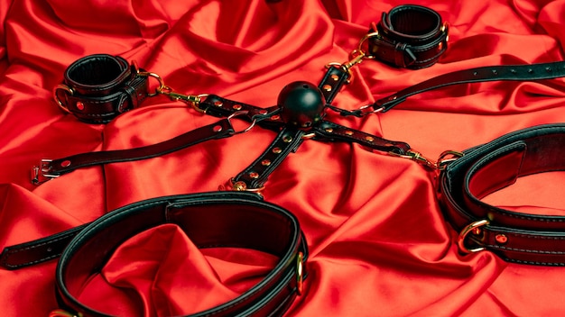 Jeux de sexe pour adultes Articles BDSM Sangles de cuir menottes et boule de bâillon sur une feuille de satin rouge