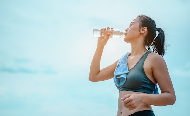 Jogger asiatique buvant de l'eau douce après l'entraînementJeune femme athlétique faisant de l'exercice sur les rochers