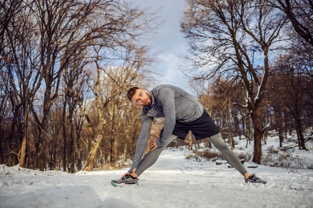 Jogger faisant des exercices d'échauffement dans la nature lors d'une journée d'hiver enneigée. Sports d'hiver, temps enneigé, exercices d'échauffement