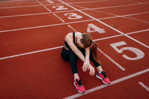 Jogger femme fatiguée assis sur le sol, stade