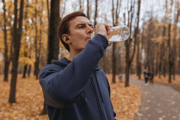 jogger masculin buvant de l'eau à partir d'une bouteille en plastique réutilisable tout en faisant une pause pendant la course