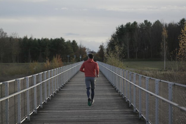 Photo jogging de cross-country dans la campagne homme en sweat-shirt orange traversant un pont en bois dans la nation