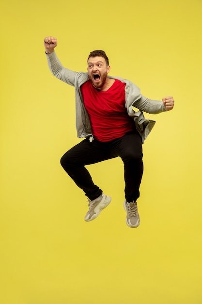 Joie. Portrait de toute la longueur du jeune homme de saut en hauteur gesticulant isolé sur fond de studio jaune. Modèle caucasien masculin attrayant. Espace de copie. Émotions humaines, concept d'expression faciale.