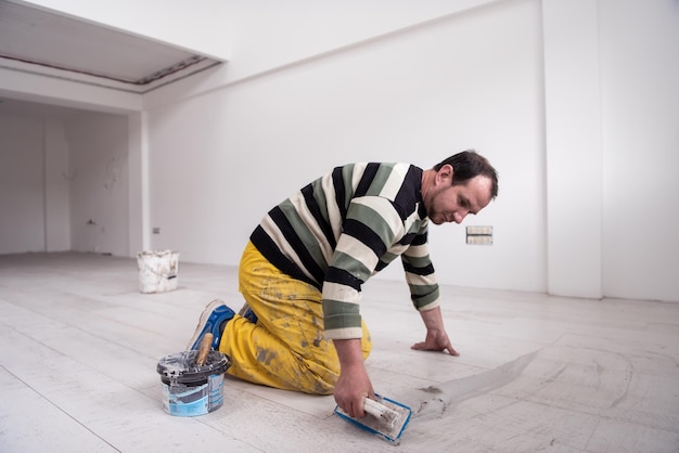 Jointoiement de carreaux de céramique. Carreleurs remplissant l'espace entre les carreaux en céramique effet bois à l'aide d'une truelle en caoutchouc sur le sol dans un nouvel appartement moderne