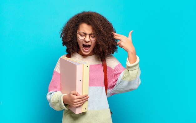 Joli adolescent afro à l'air malheureux et stressé, geste de suicide faisant un signe d'arme à feu avec la main, pointant vers la tête. concept d'étudiant