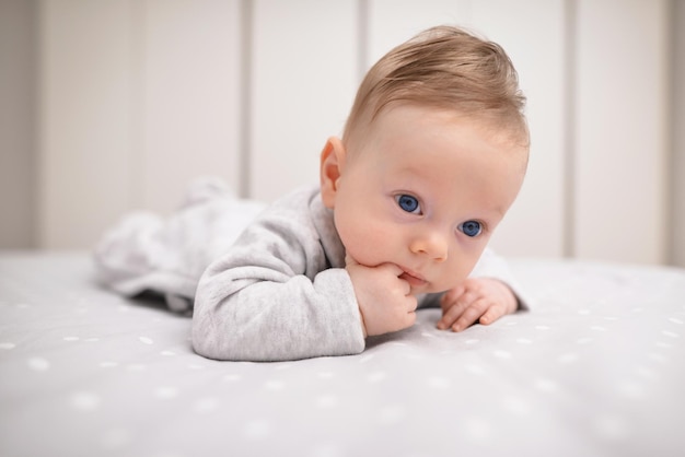 Joli bébé allongé sur un drap blanc et garde les doigts dans sa bouche Concept d'enfance heureuse