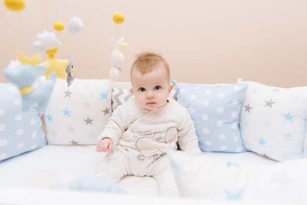 Joli bébé assis dans un lit rond blanc. Garderie légère pour jeunes enfants. Jouets pour lit bébé. Enfant souriant jouant avec mobile de feutre dans une chambre ensoleillée.