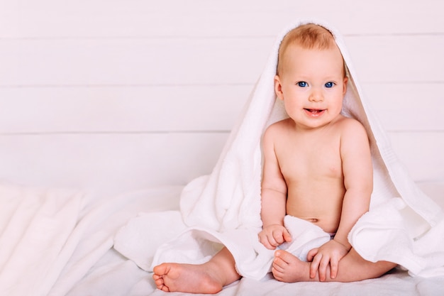 Un joli bébé aux yeux bleus enveloppé dans une serviette blanche alors que la capuche regarde dans l'appareil photo.