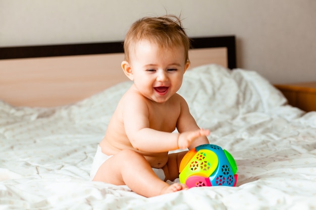 Joli bébé blond jouant avec un ballon assis sur le lit dans la chambre. heureux bébé de 6 mois jouant avec un ballon