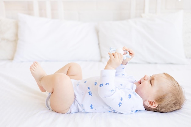 Joli bébé avec une bouteille de lait suce en le tenant dans ses mains allongé sur le dos sur un lit de bébé dans une chambre lumineuse pour enfants concept d'aliments pour bébés