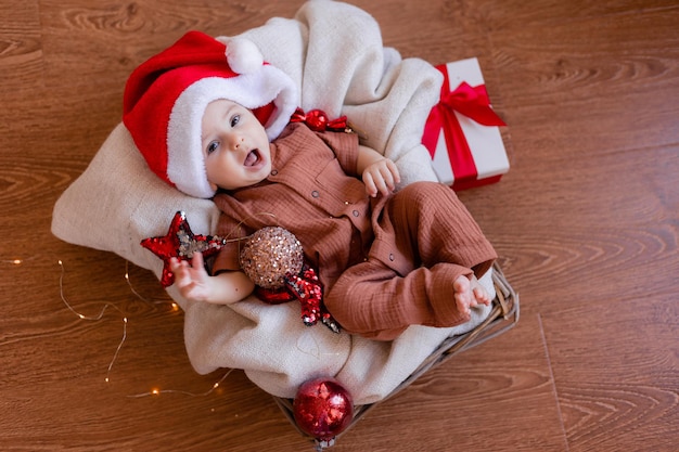 Joli bébé dans un bonnet de Noel est allongé dans une couverture sur le sol et tient une boule de Noël dans sa main. joyeuses fêtes. hiver, nouvel an. Photo de haute qualité