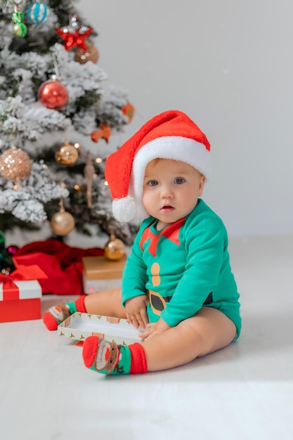 Joli bébé dans un costume de gnome de Noël ouvre des cadeaux près de l'arbre de Noël. produits pour enfants et vacances. concept du nouvel an d'hiver. espace pour le texte. Photo de haute qualité