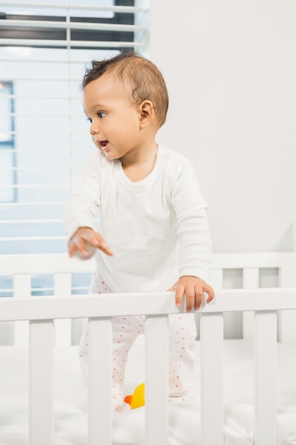 Joli bébé debout dans le lit dans la chambre