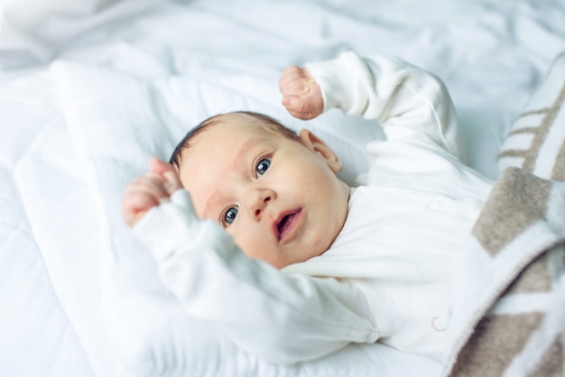 Joli bébé drôle allongé sur un lit blanc recouvert d'une couverture