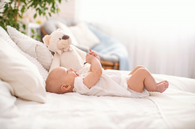 Joli bébé est allongé sur le dos sur le lit et joue avec ses mains