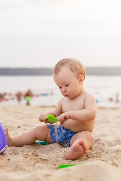 Joli bébé est assis dans le sable et joue avec des jouets au bord de la mer