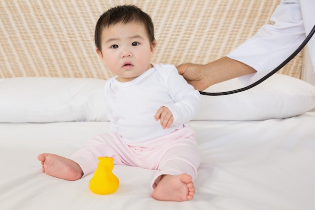 Joli bébé sur le lit et la main du médecin lui rendant visite