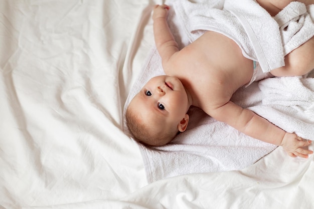 Joli bébé nouveau-né enveloppé dans une serviette blanche se trouve sur un lit avec des sous-vêtements en coton blanc. propreté, hygiène. produits pour enfants. concept d'enfance et de maternité heureuses. garde d'enfants. espace pour le texte