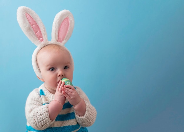 Joli bébé portant des oreilles de lapin de pâques jouant avec un œuf de pâques