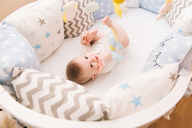 Joli bébé se trouve dans un lit rond blanc. Garderie légère pour les jeunes enfants.