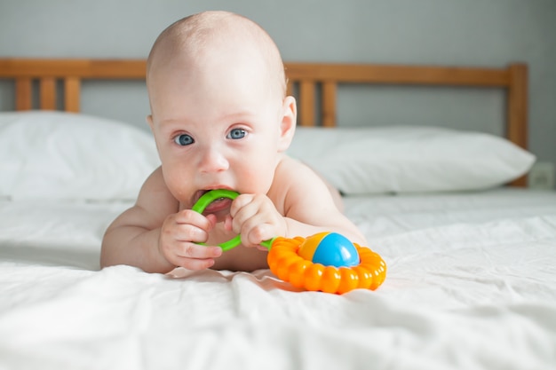 Un joli bébé se trouve sur un drap blanc et joue gaiement avec un hochet lumineux