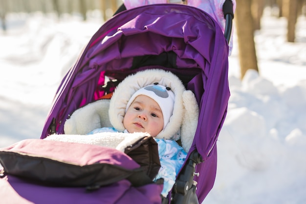 Joli bébé souriant assis dans une poussette par une froide journée d'hiver.