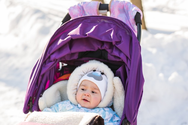 Joli bébé souriant assis dans une poussette par une froide journée d'hiver.