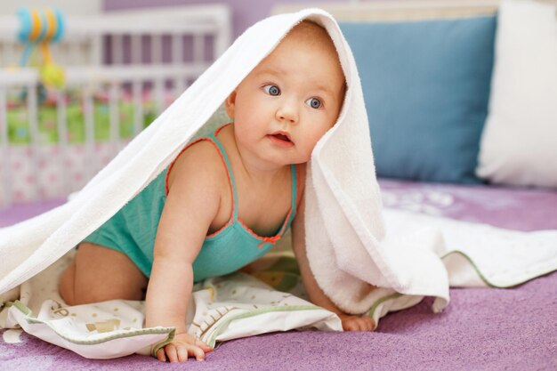 Joli bébé souriant regardant la caméra sous une serviette blanche portrait d'un enfant mignon