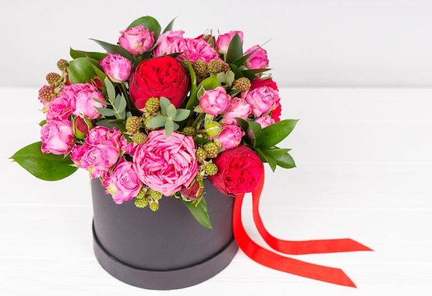 Joli bouquet de roses roses et rouges et ruban rouge dans une boîte noire circulaire sur une table en bois blanche. Concept de la Saint-Valentin et anniversaire