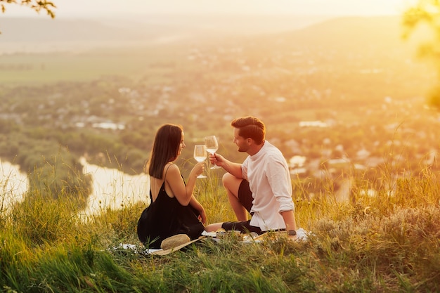 joli couple appréciant un pique-nique romantique au coucher du soleil sur la colline.