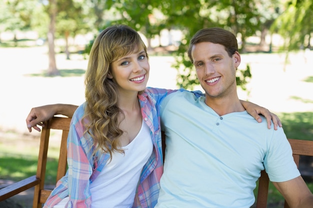 Joli couple assis sur un banc dans le parc, souriant à la caméra