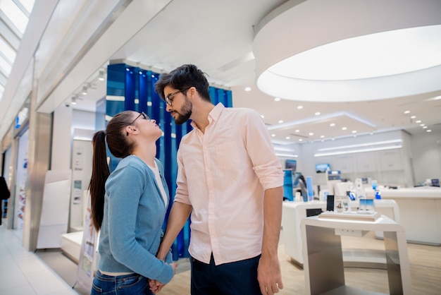 Joli couple debout dans le magasin de technologie et main dans la main. Concept de technologies de nouvel âge.