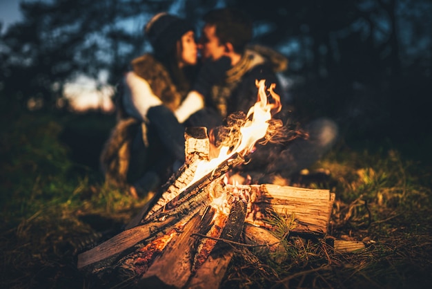 Joli couple de détente près de feu de joie dans la forêt au moment de la soirée