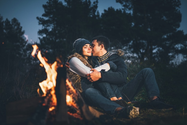 Joli couple de détente près de feu de joie dans la forêt au moment de la soirée