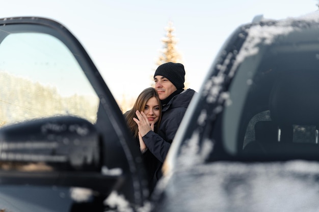 Joli couple étreignant près de la voiture en hiver homme et femme amoureux se regardent près de la voiture